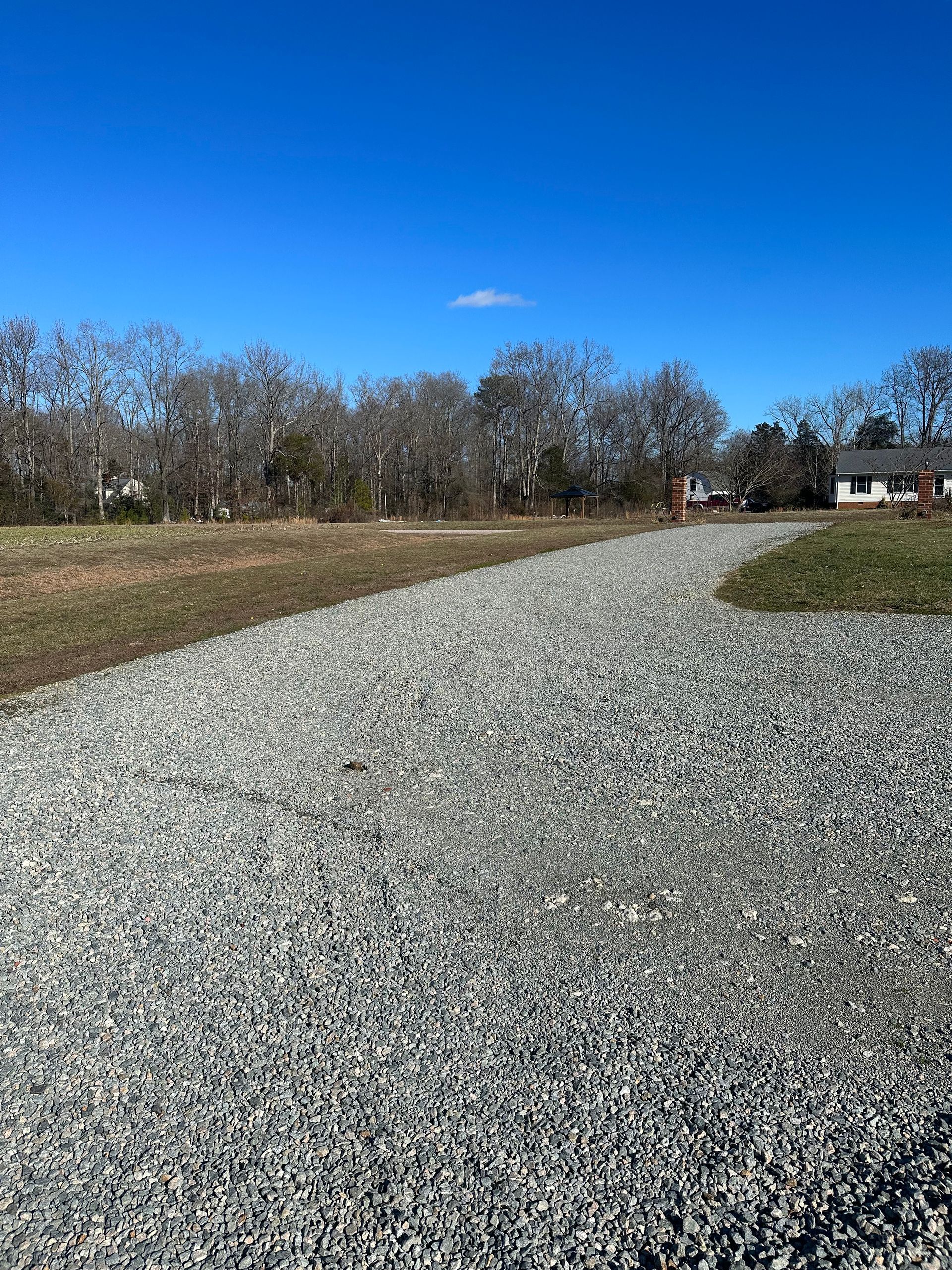 A gravel road going through a field with trees in the background.