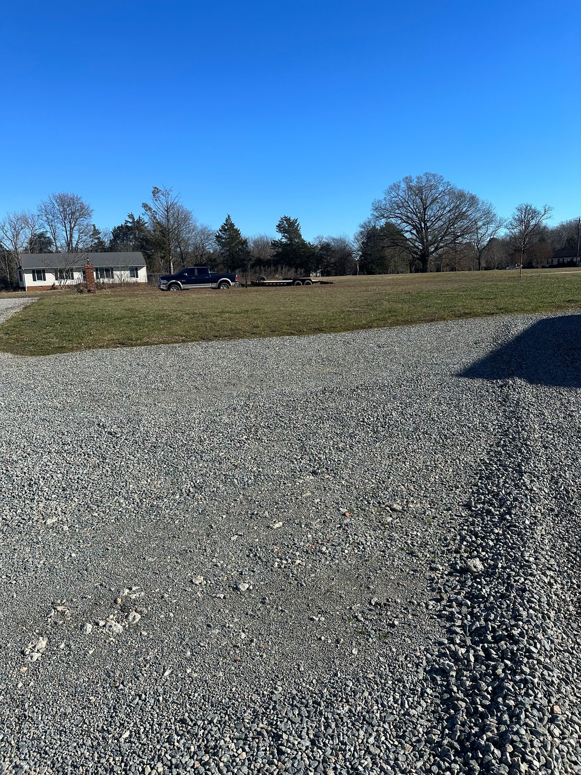 A gravel road leading to a field with a house in the background.