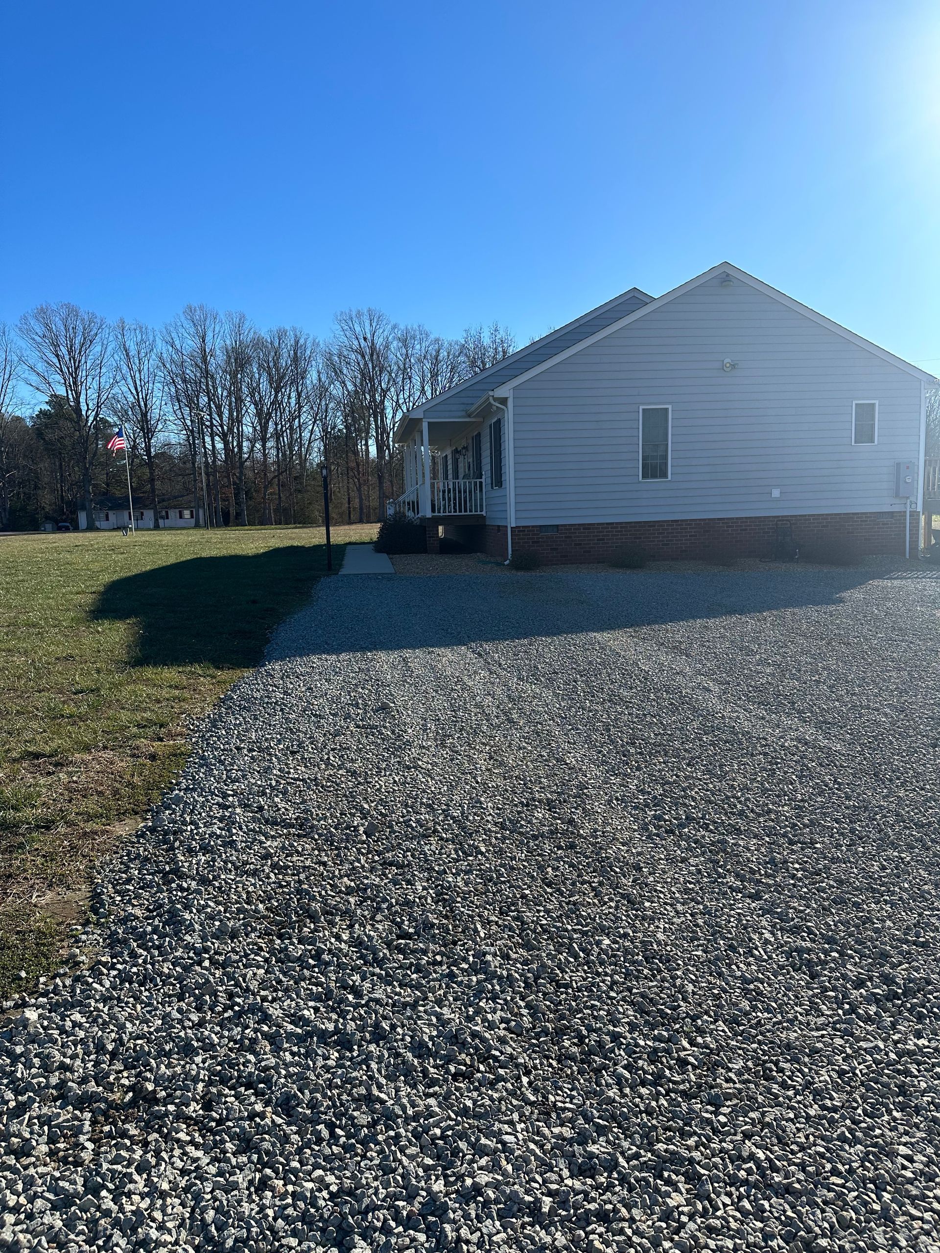 A white house is sitting in the middle of a gravel driveway.