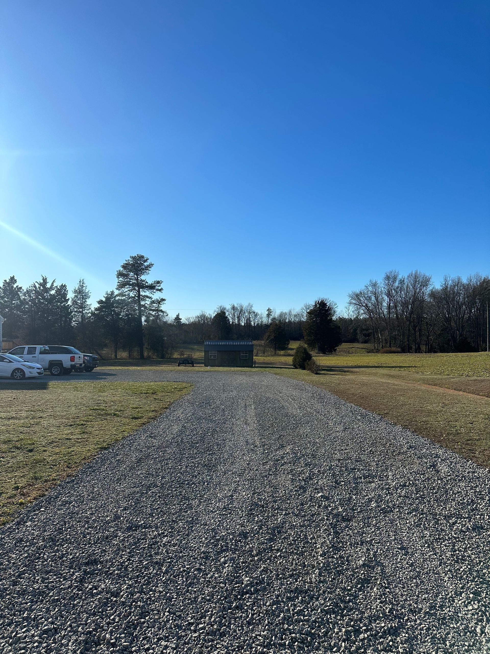 A gravel road going through a field with a blue sky in the background.