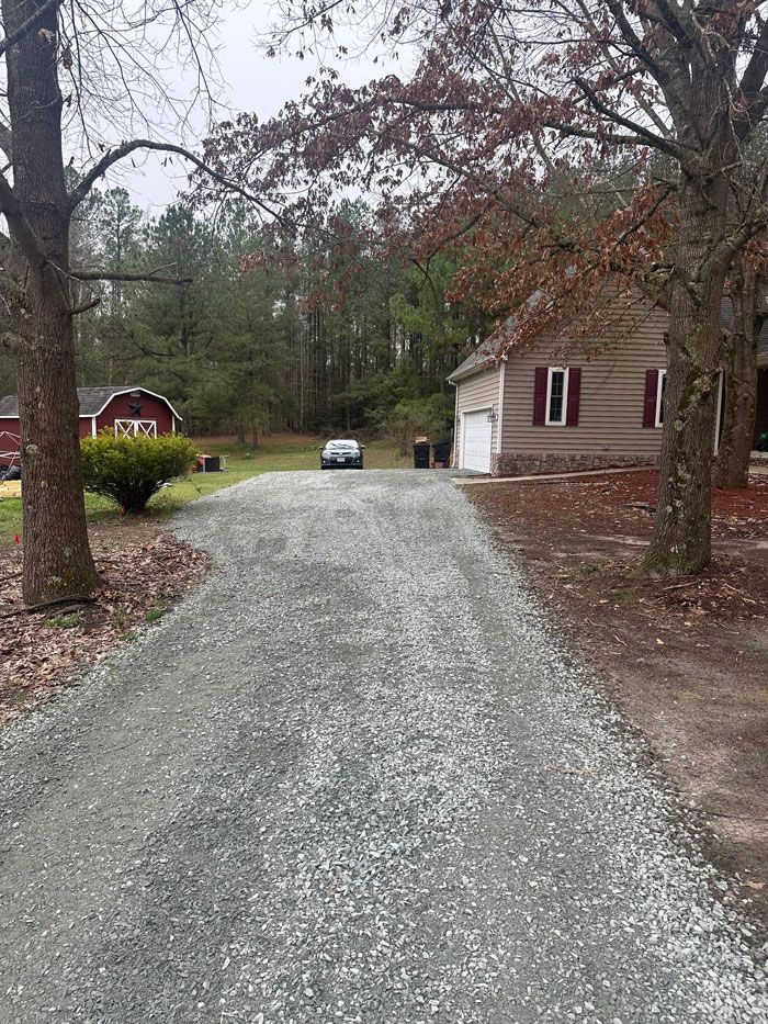 A gravel driveway leading to a house in the woods.