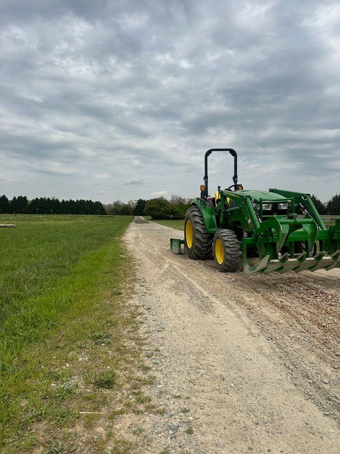 A green tractor is driving down a dirt road in a field.