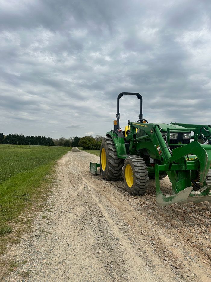 A green tractor is parked on the side of a dirt road.