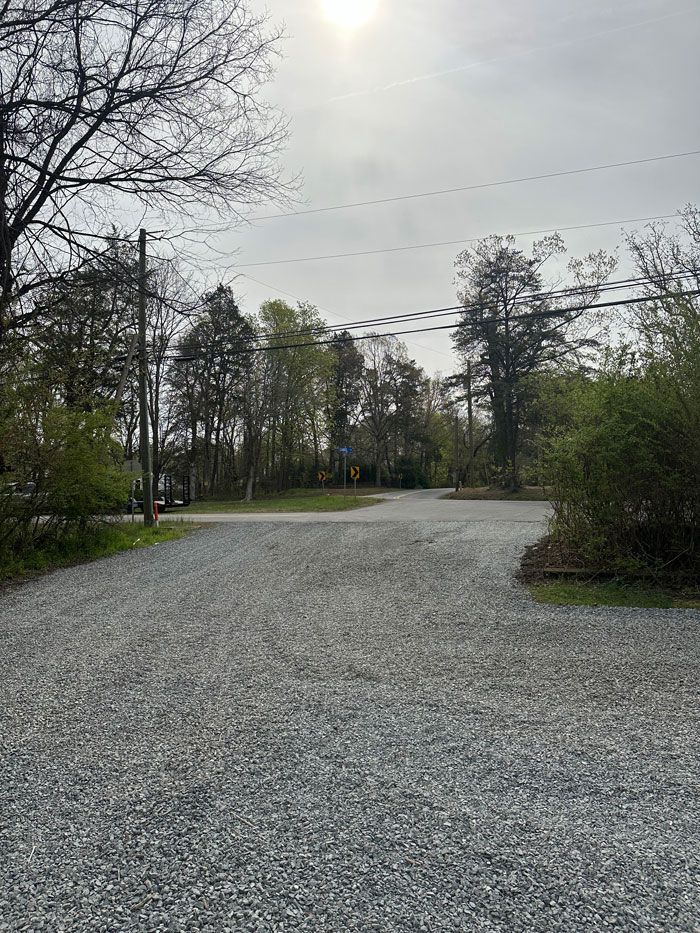 A gravel road surrounded by trees and power lines on a cloudy day.