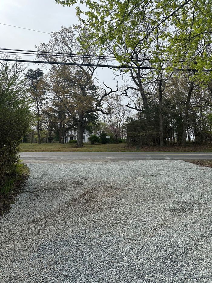 A gravel driveway leading to a house with trees in the background.
