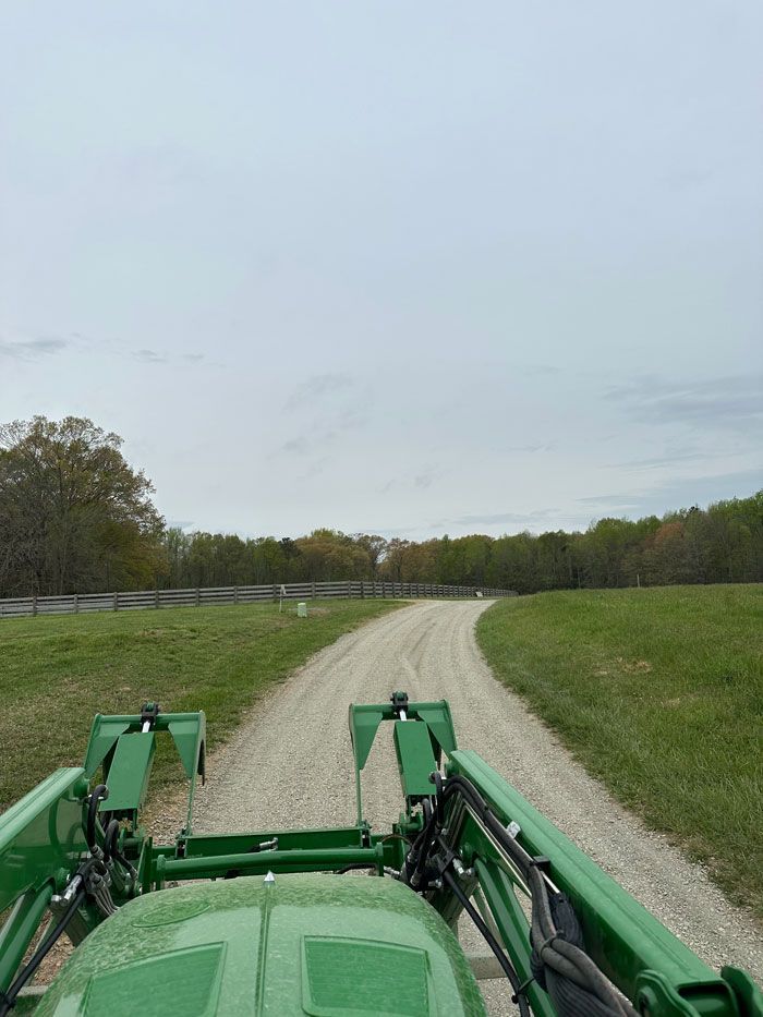 A green tractor is driving down a dirt road.