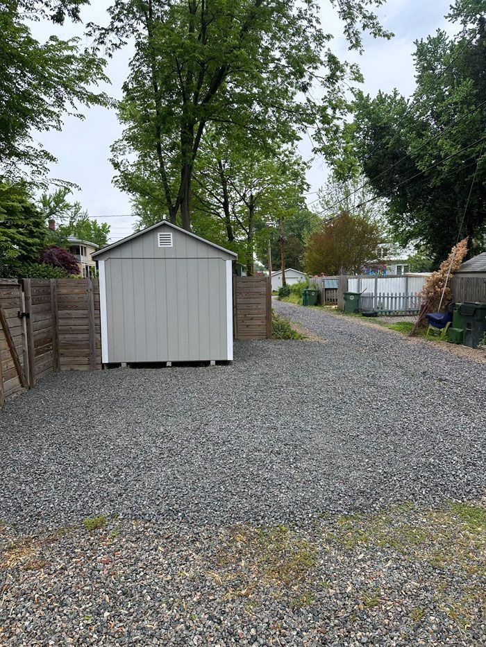 A shed is sitting in the middle of a gravel driveway.