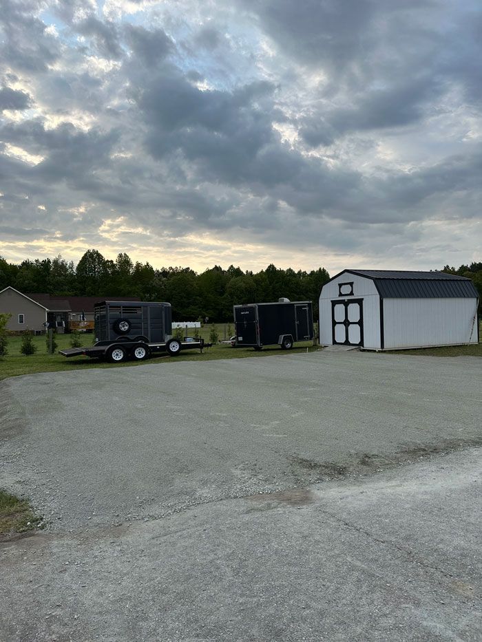 A trailer is parked in a gravel lot next to a barn.