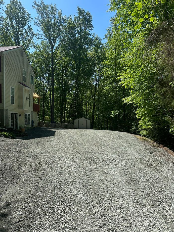 A gravel driveway leading to a house surrounded by trees on a sunny day.