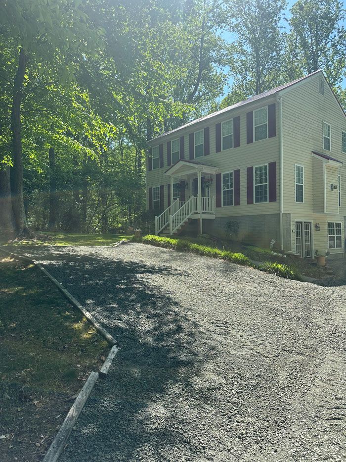 A large white house with a gravel driveway in front of it surrounded by trees.