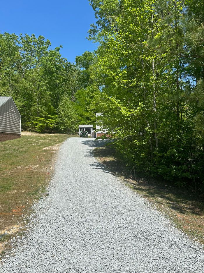A gravel driveway leading to a house surrounded by trees on a sunny day.