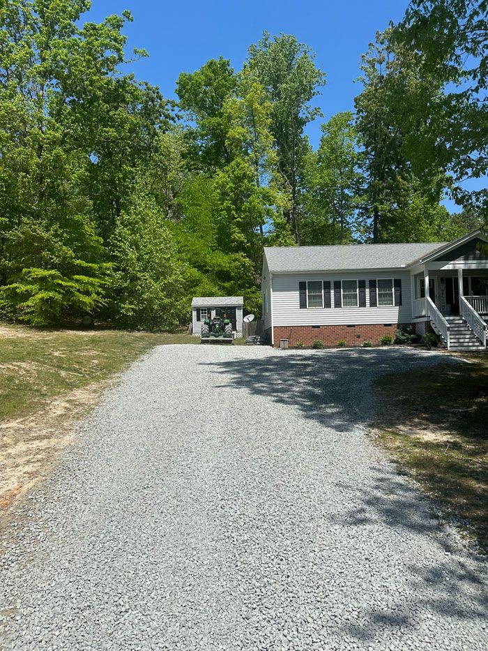 A white house with a gravel driveway leading to it is surrounded by trees.