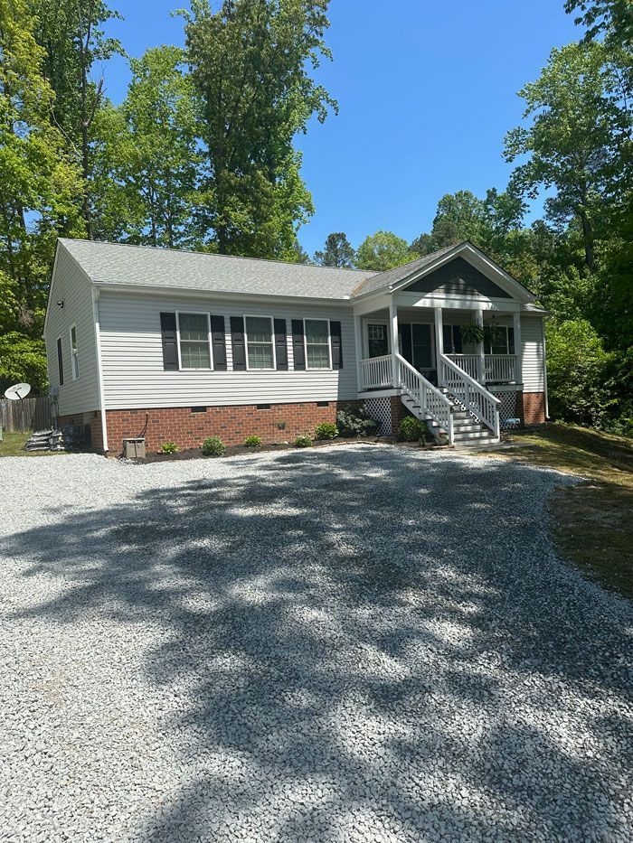 A white house with a gravel driveway in front of it surrounded by trees.