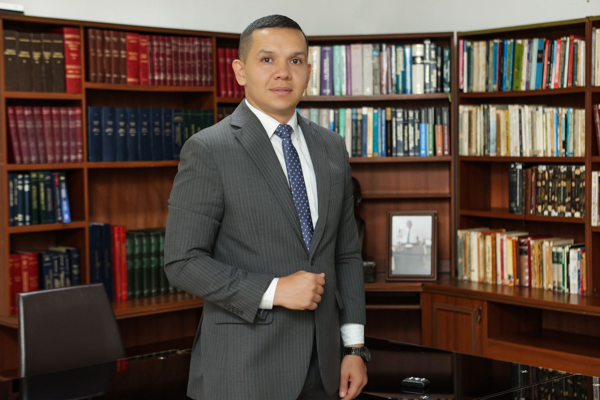 Un hombre con traje está de pie en una biblioteca, mirando a la cámara.