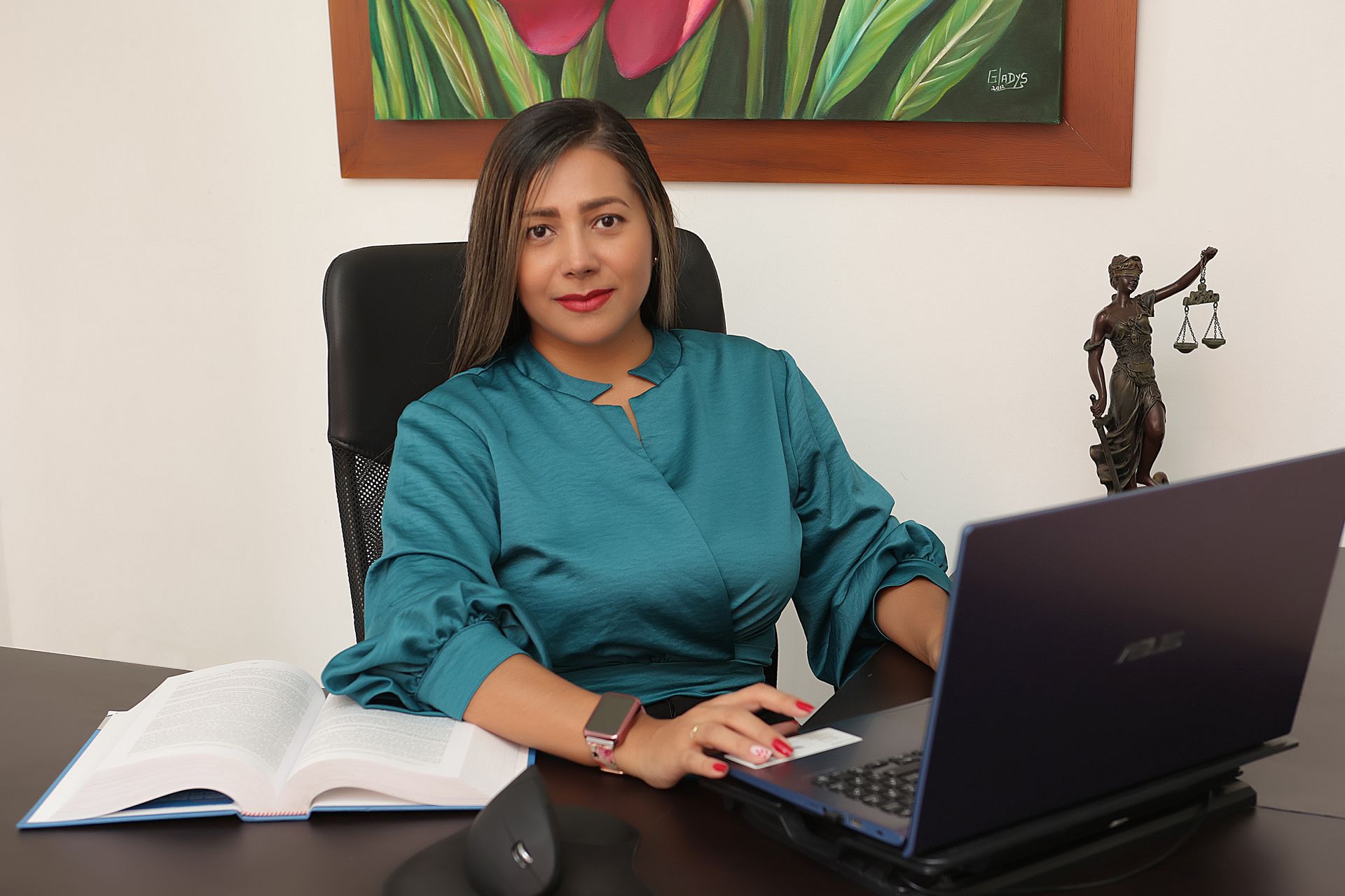 Mujer sentada en un escritorio con computadora portátil, libro abierto y estatua de la justicia; 