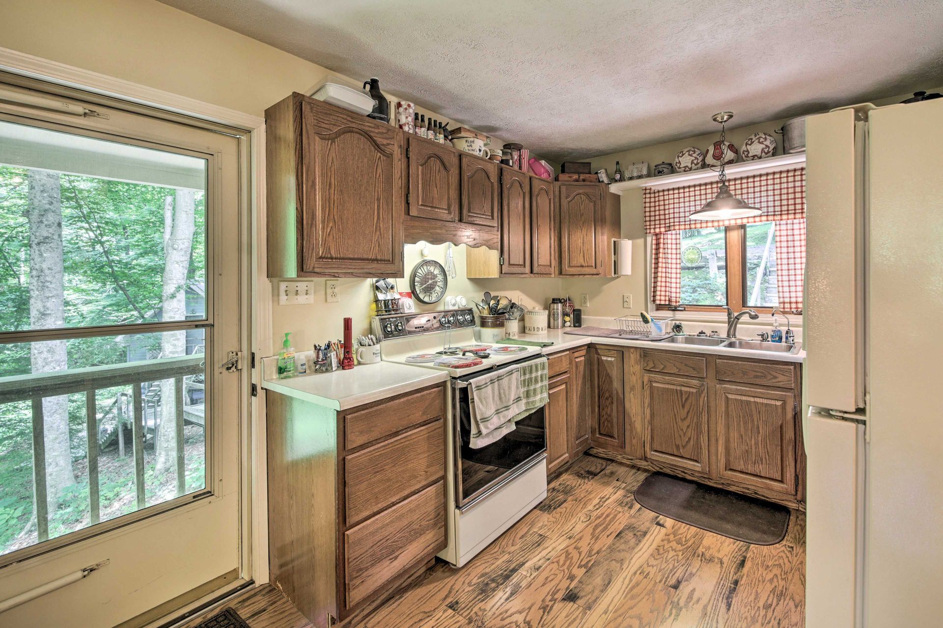 Kitchen with wood cabinets, white appliances, and a door leading to a balcony overlooking trees.