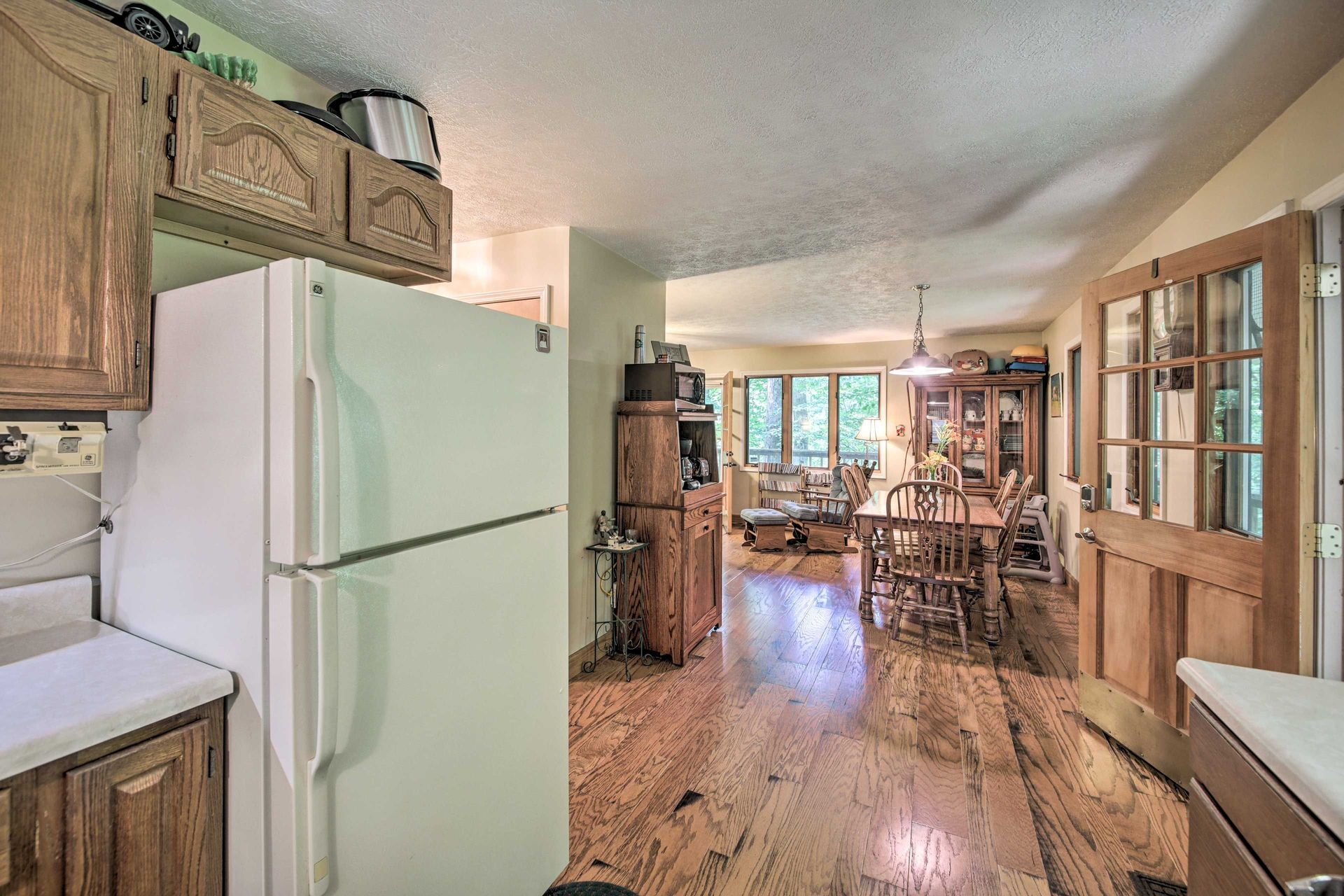 Kitchen with white refrigerator, wooden cabinets, and a view into a dining area with wood floors.