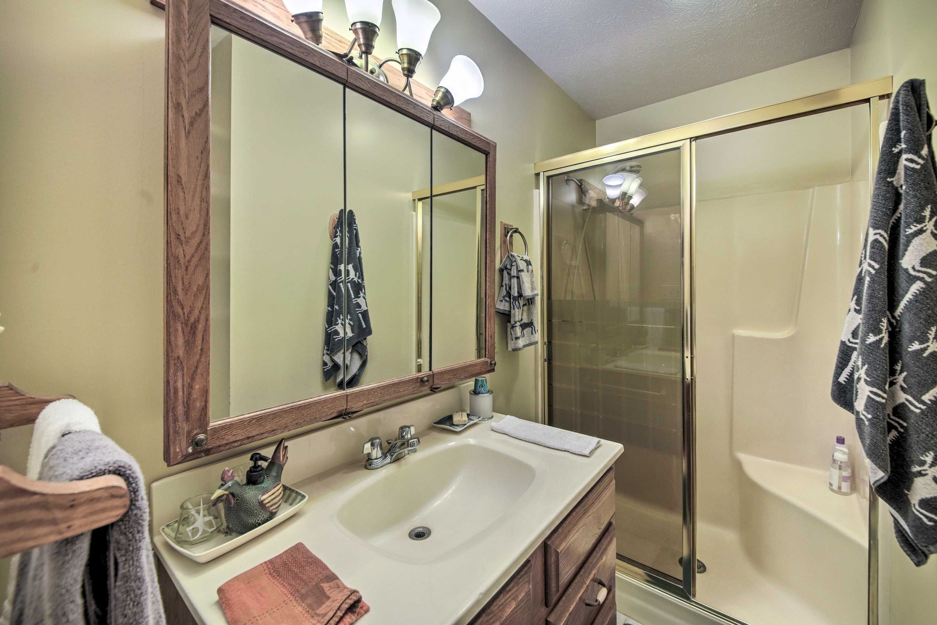 Bathroom with vanity, mirror, and shower. Brown cabinetry and trim.  Towels hung on the wall and shower door.