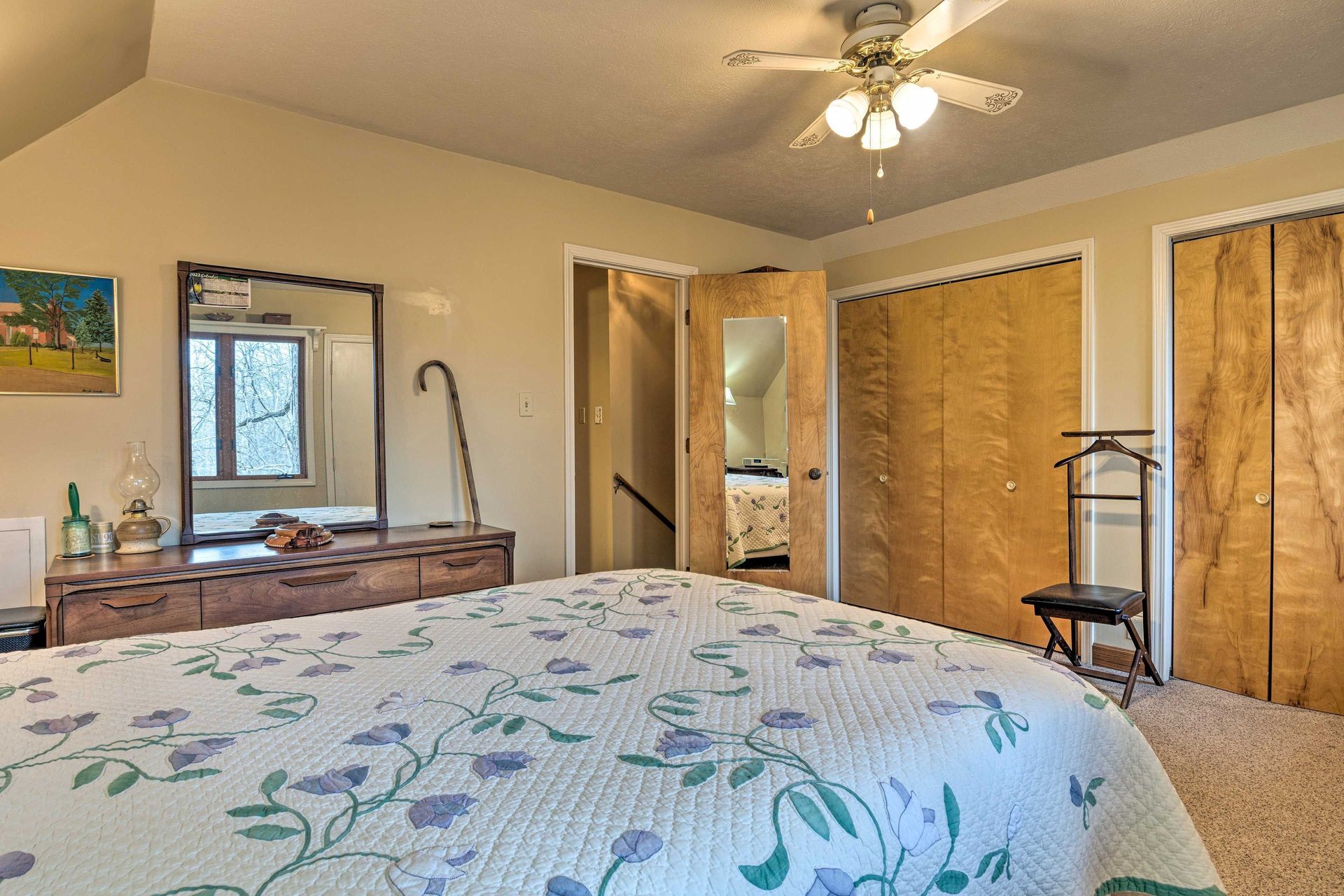 Bedroom with bed, dresser, mirror, closets, doorway, and ceiling fan.