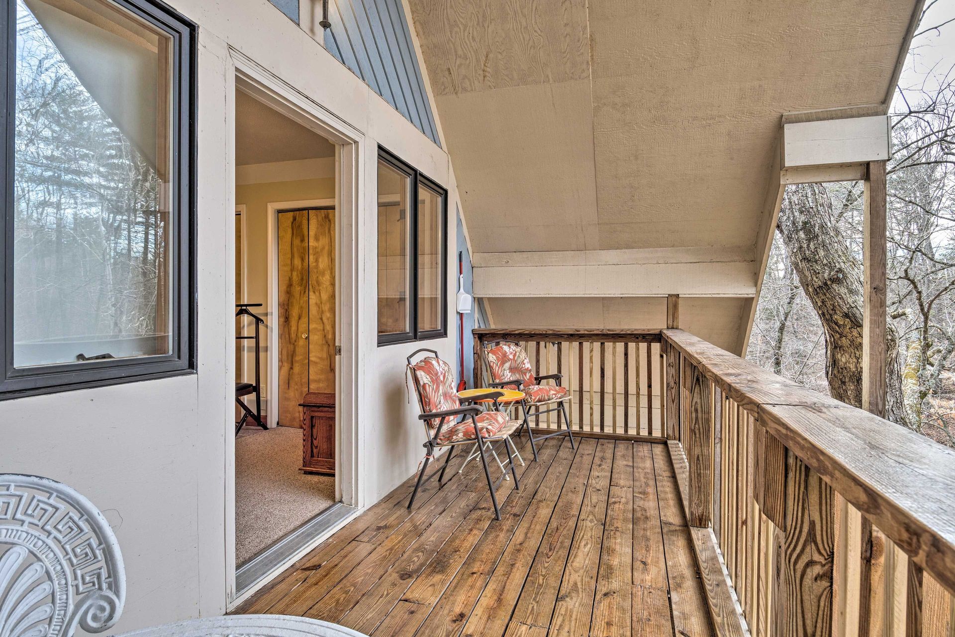 Wooden deck with chairs and a doorway leading indoors; trees visible.