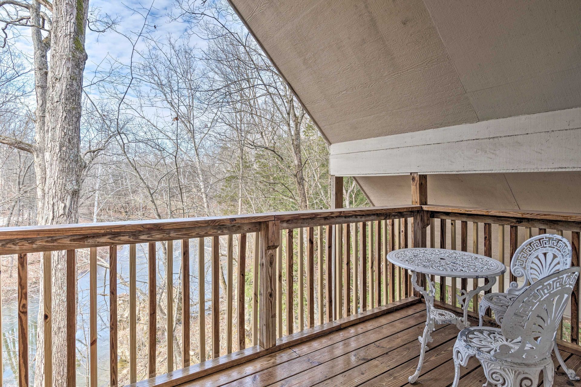 Wooden deck with white table and chairs, overlooking a forest and water.
