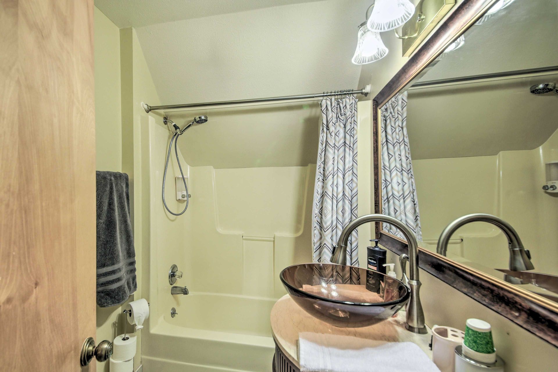 Bathroom with a glass vessel sink, bathtub/shower, and grey shower curtain.
