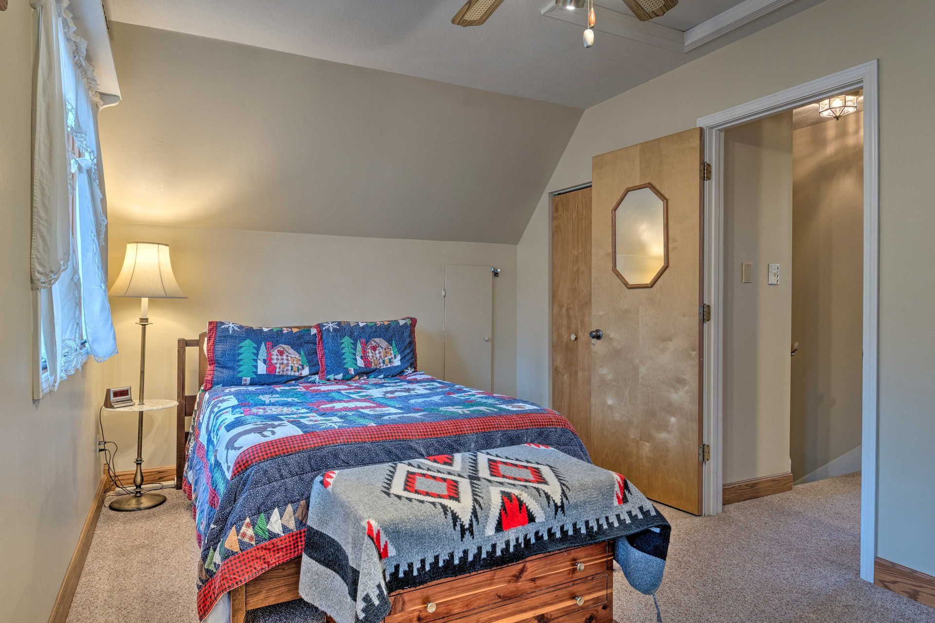 Bedroom with a bed, blanket chest, side table with lamp, and doorway to another room.