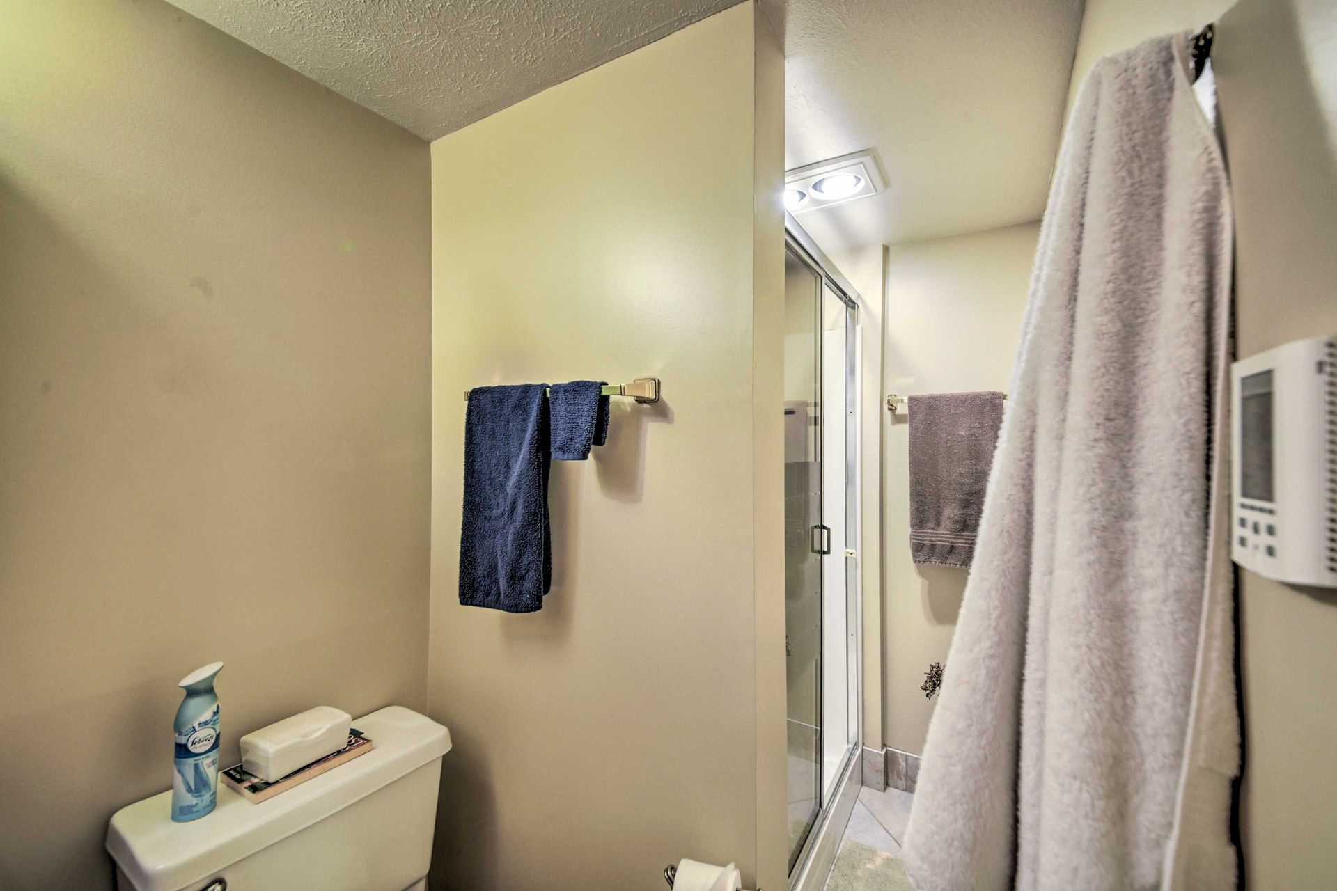 A beige bathroom with a toilet, towels, and a shower.