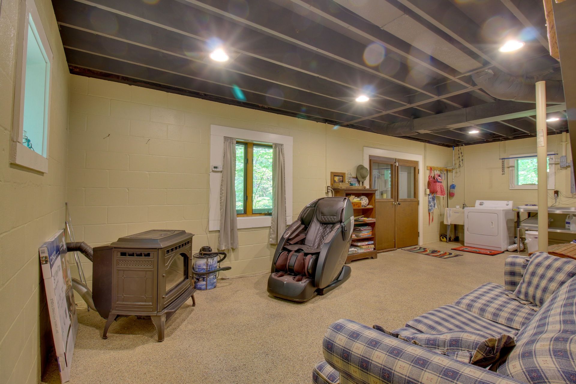 Basement living area with beige walls, black ceiling, sofa, massage chair, stove, and laundry machines.