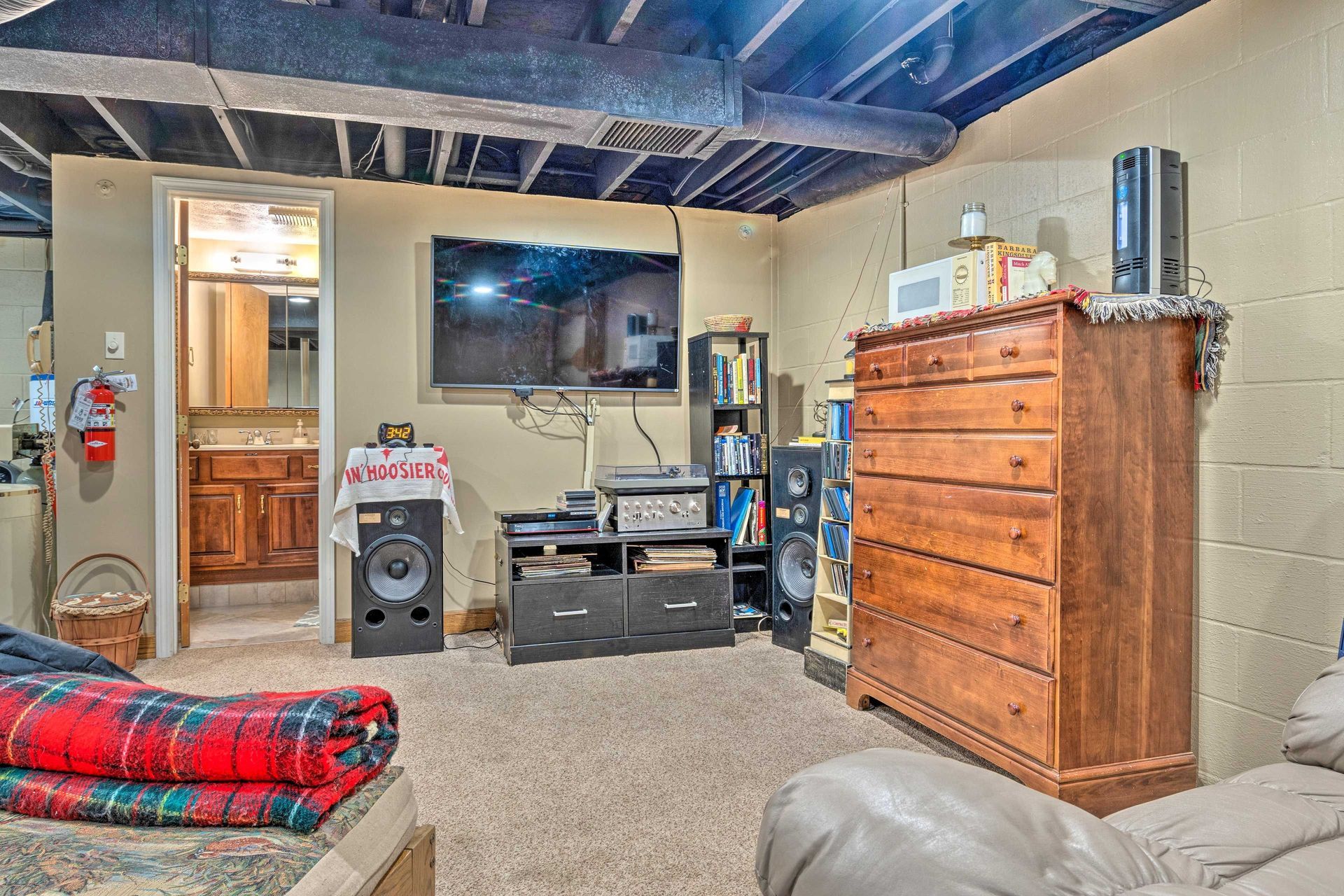 Basement with TV, stereo, speakers, a dresser, and a doorway to a bathroom.