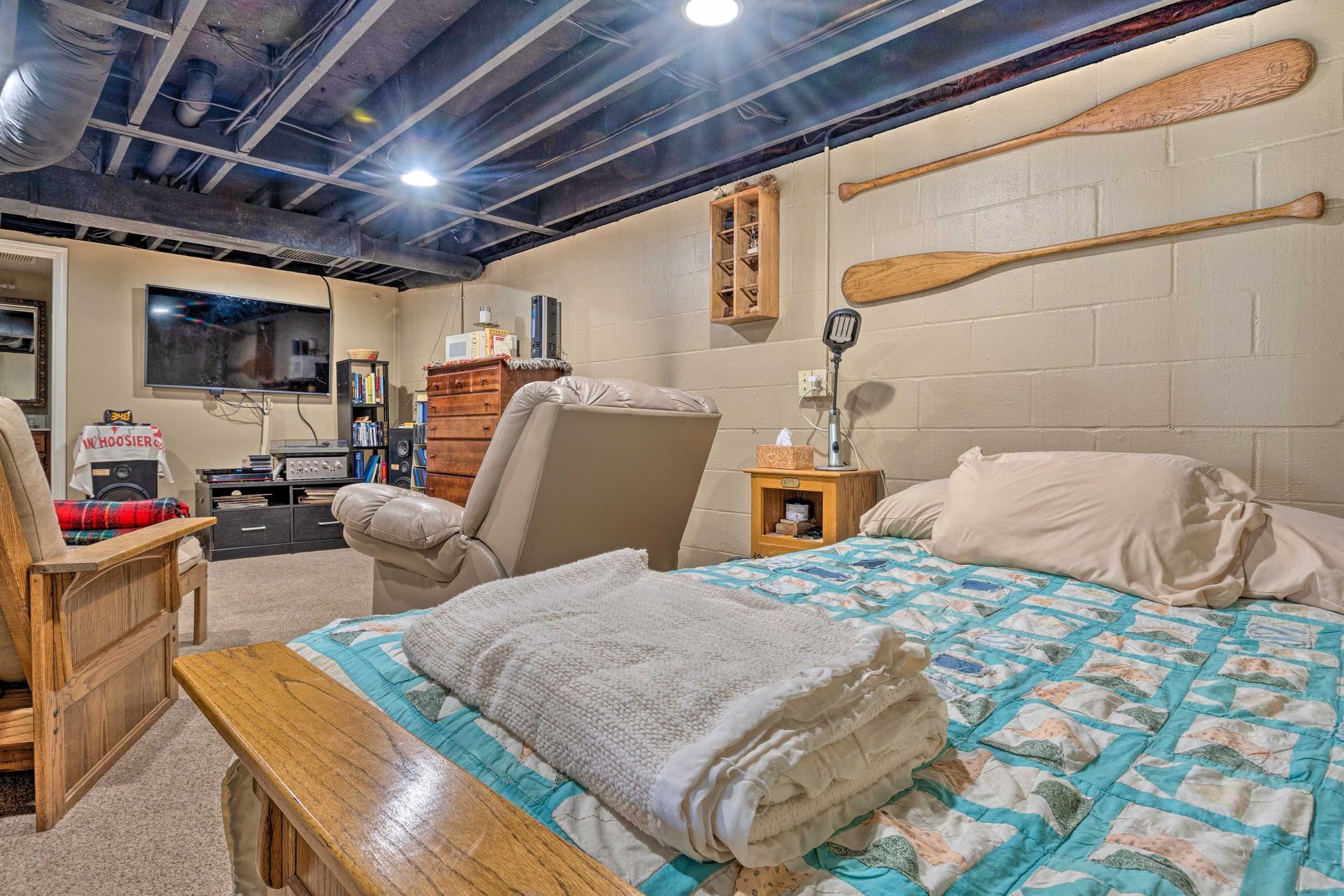 Bedroom in a basement with bed, recliner, oars on the wall, and a TV.