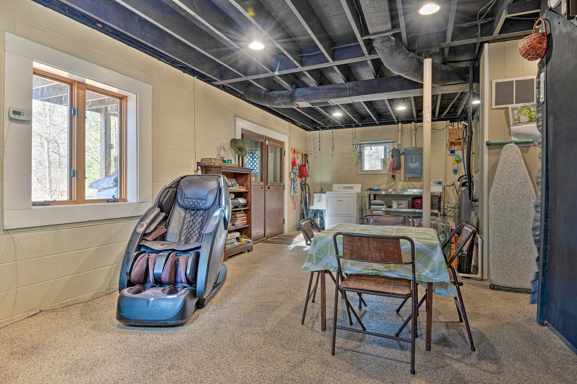 Basement room with massage chair, table, washer, and small window.