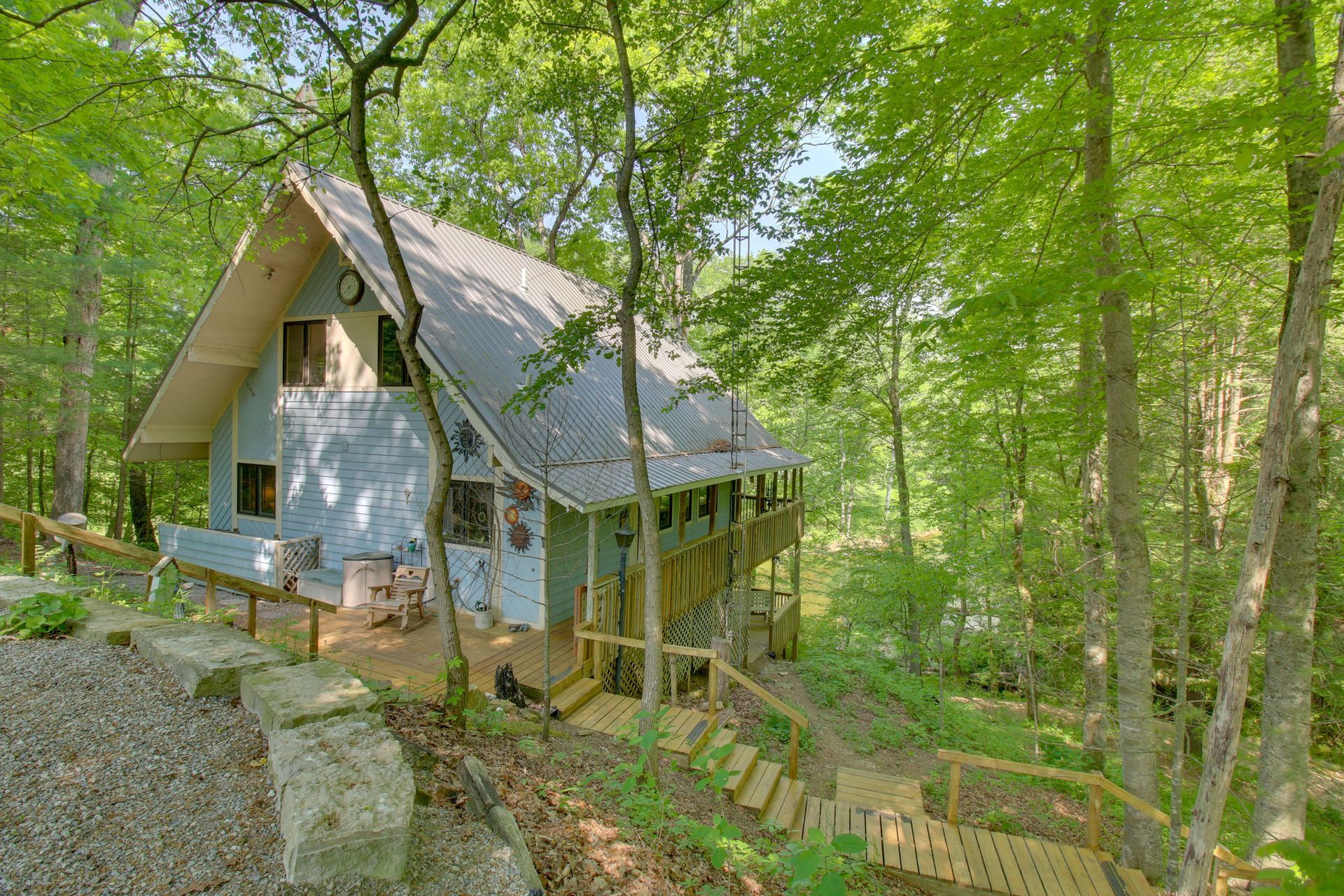 A-frame cabin nestled in a lush green forest, with a wooden walkway and steps leading to it.