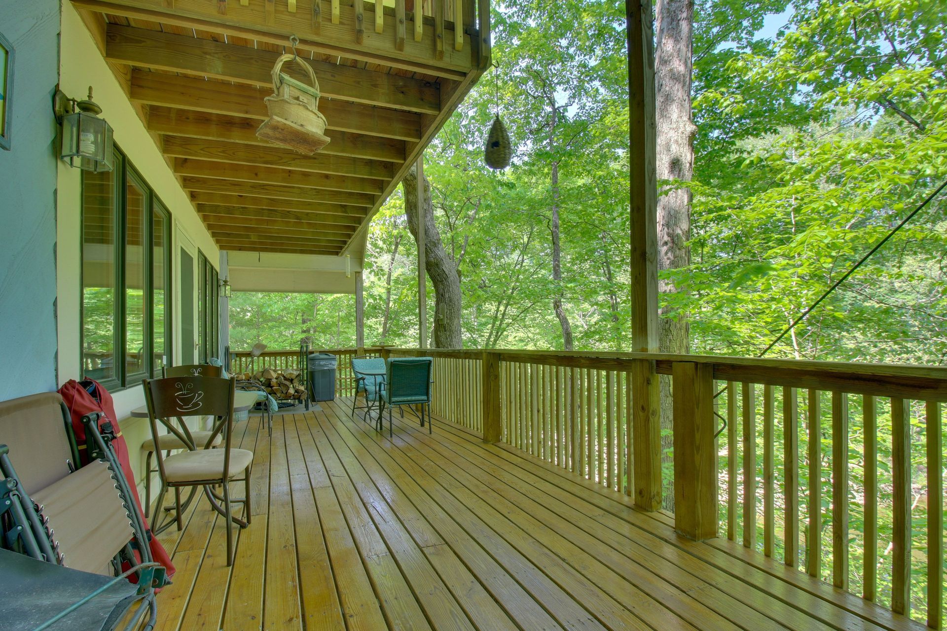 Wooden deck with chairs, surrounded by trees, beneath a balcony.