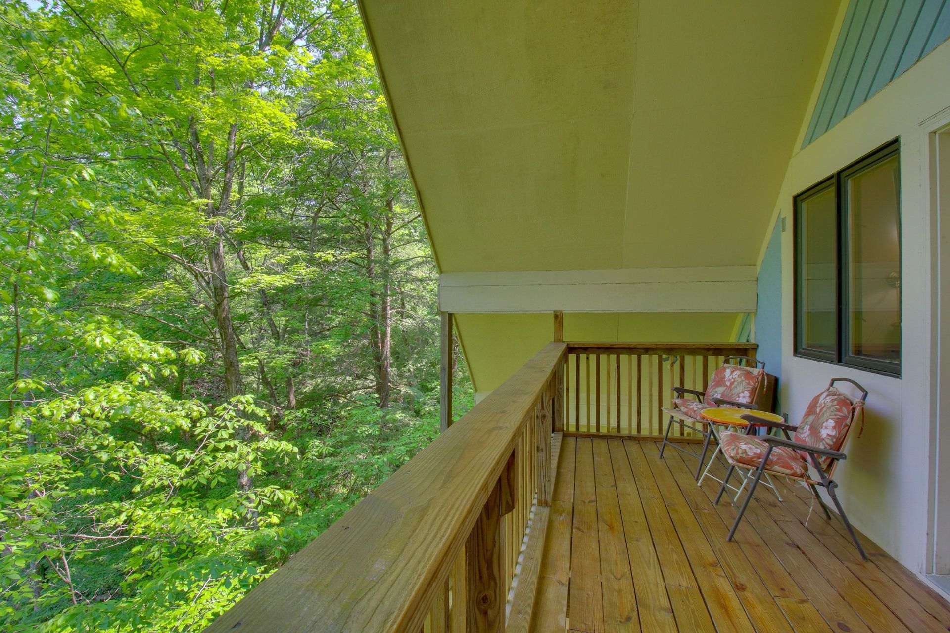 Wooden balcony with two chairs overlooking a lush green forest.