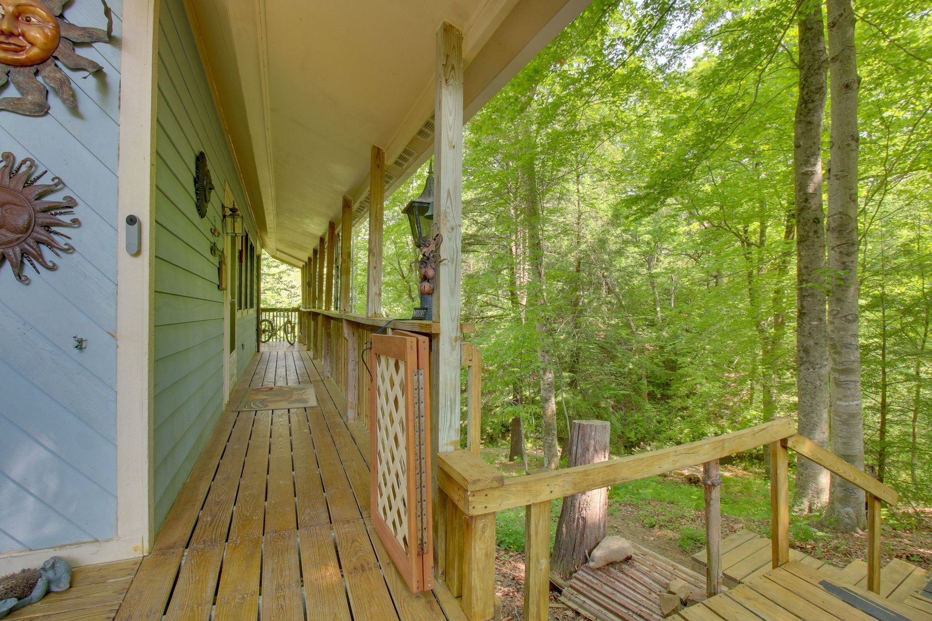 Long porch with wooden railing, leading to forest. Light blue house exterior with sun decor.