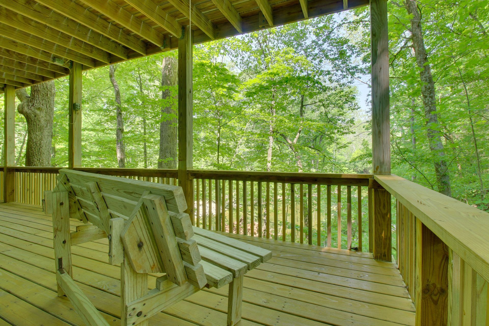 Wooden porch with swing overlooking lush green trees.
