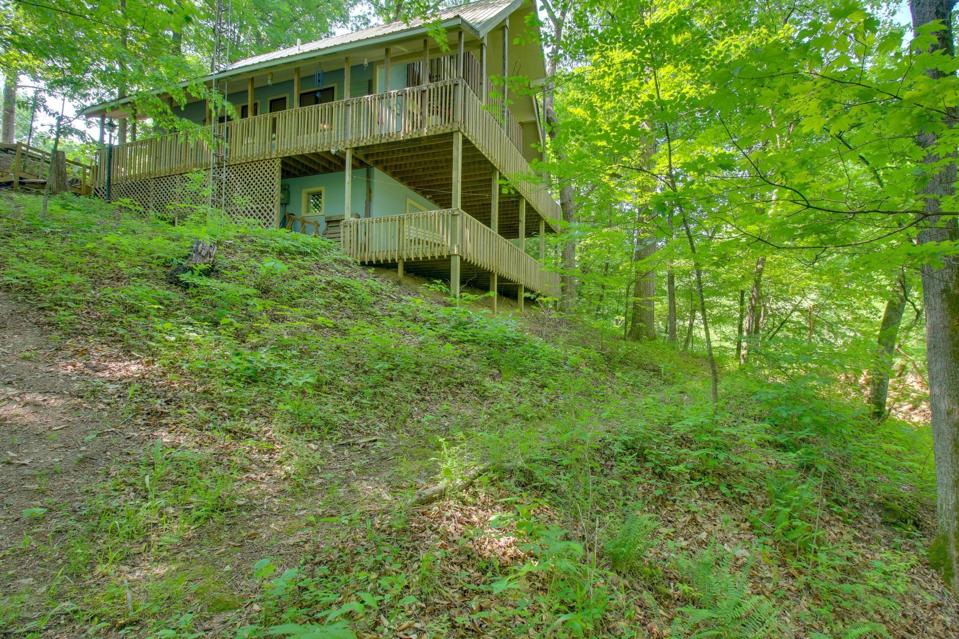 Wooden cabin nestled in a wooded hillside, with multiple decks and green foliage.