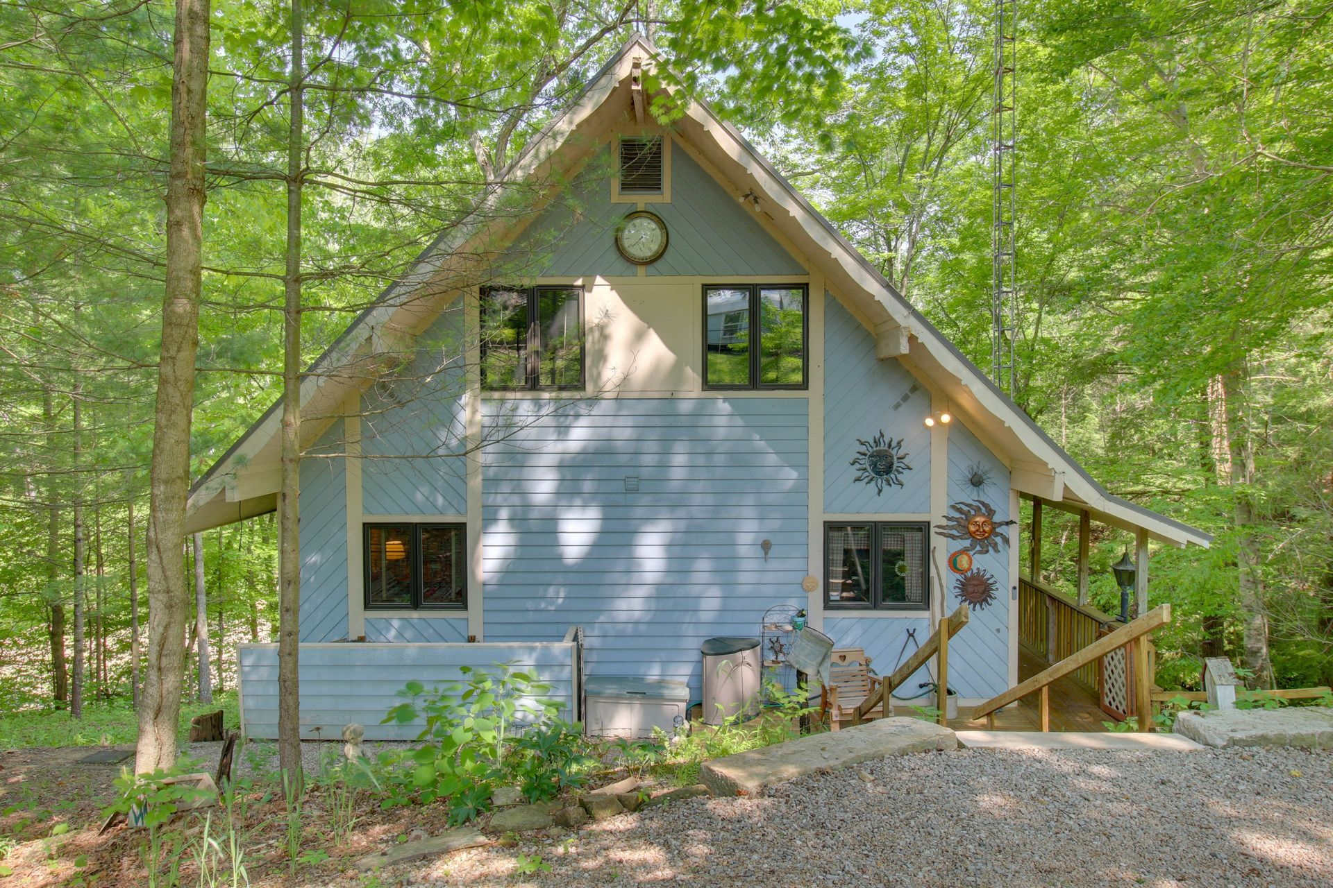 Blue A-frame cabin in a wooded setting with artistic sunburst decorations.