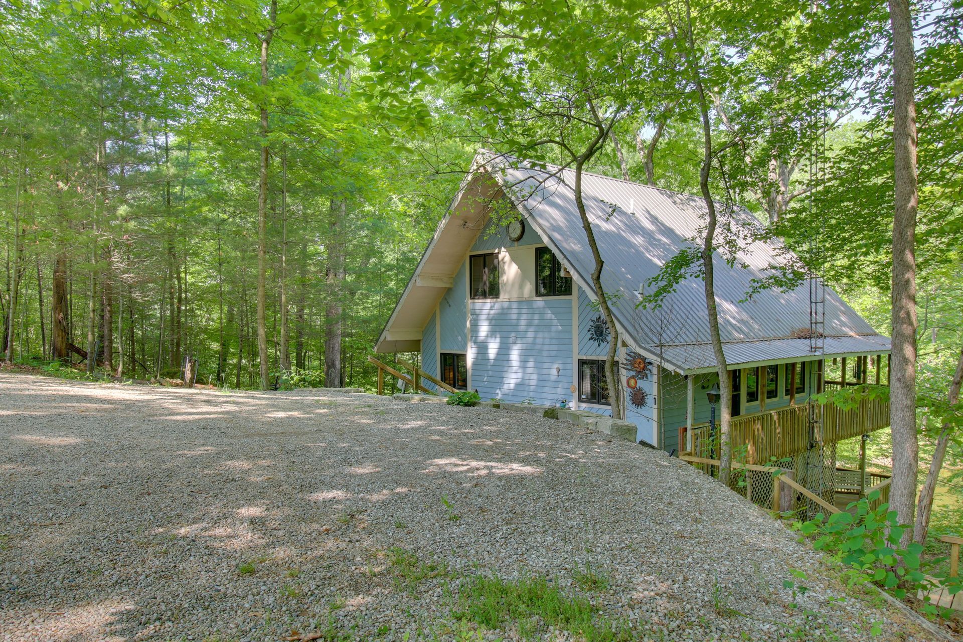 Blue cabin in a wooded area with a gravel driveway.