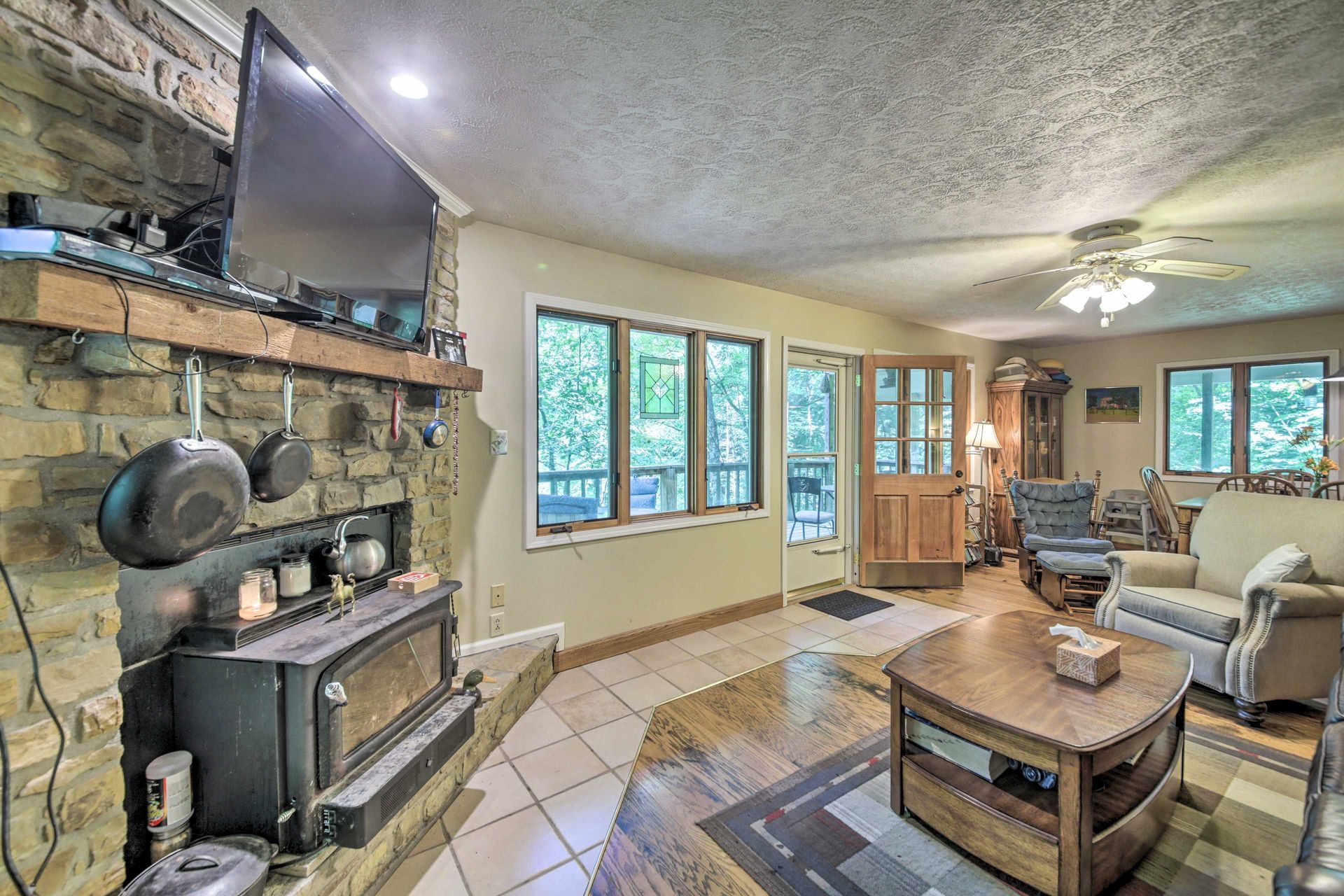Cozy living room with stone fireplace, wood-burning stove, TV, windows, and comfortable seating.