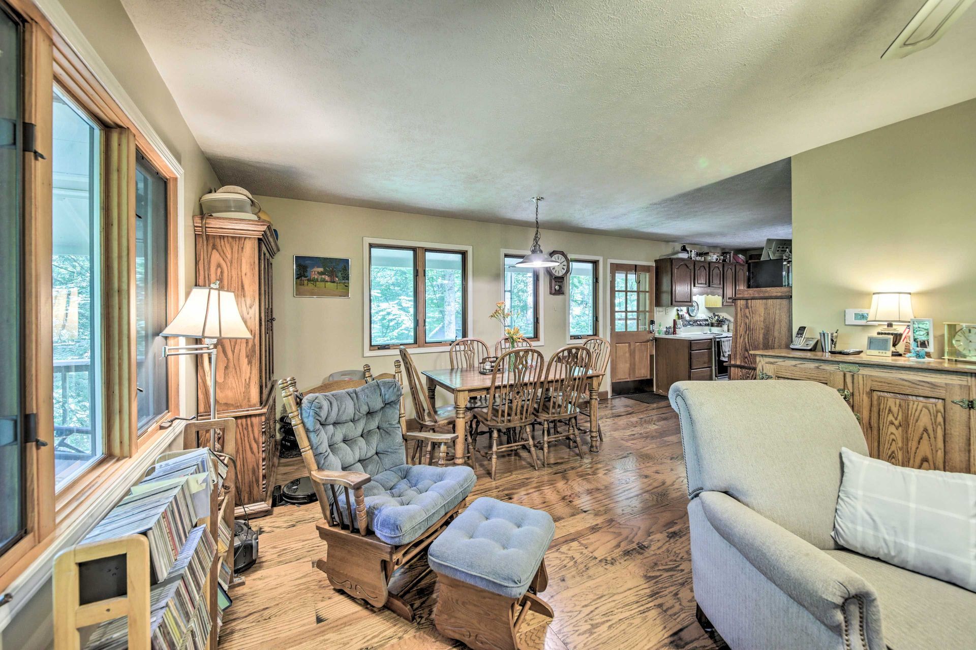 Spacious living room with rocking chair, dining area, and kitchen; windows throughout.