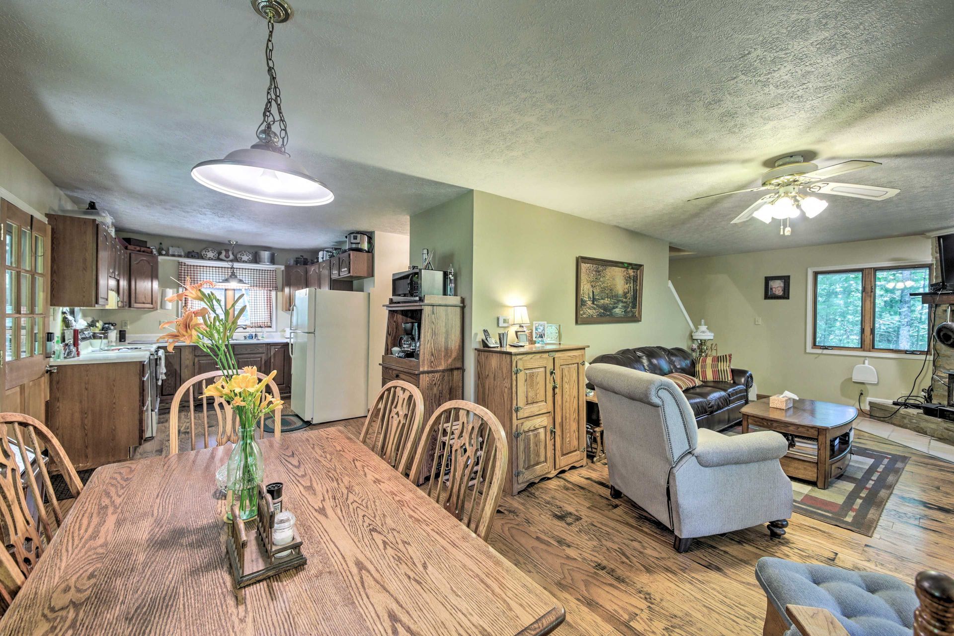 Open-concept dining room, kitchen, and living room. Wood floors, dining table, chairs, cabinets, appliances, couch.