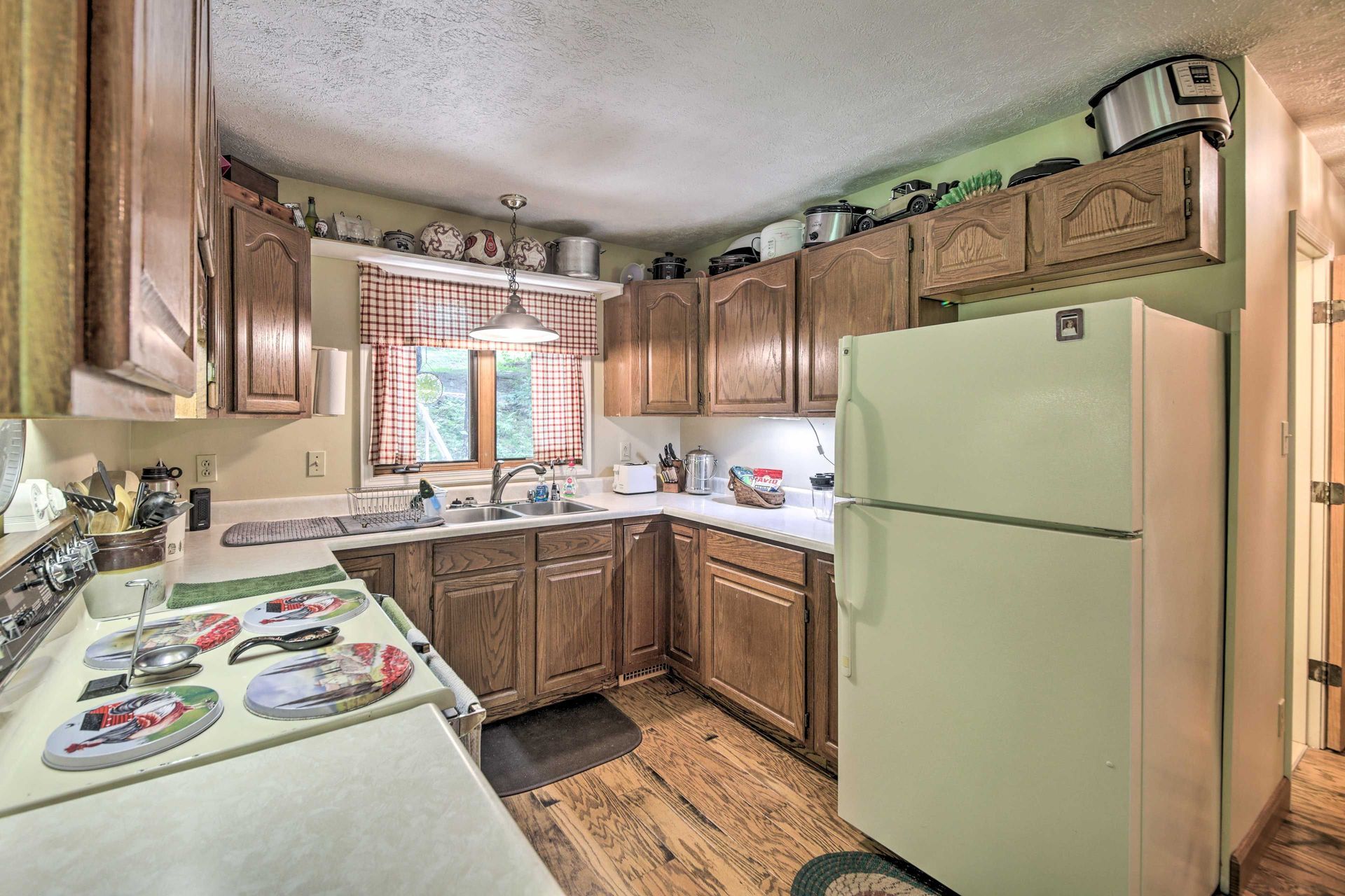 Kitchen with wooden cabinets, white refrigerator, window with curtains, and various kitchen items.