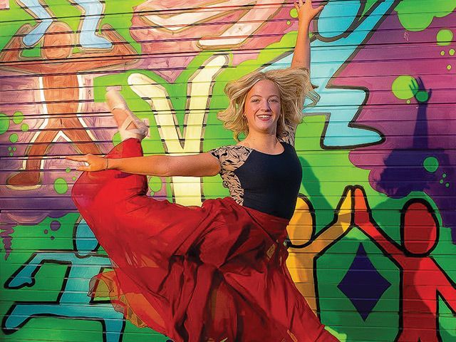 A woman is dancing in front of a colorful graffiti wall.