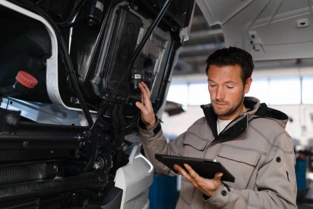 Mechanic inspecting vehicle engine while holding a tablet.