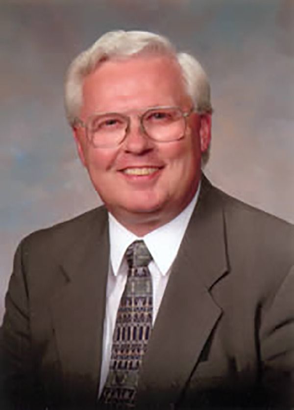 Man in suit and tie smiling, wearing glasses.