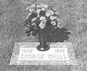 Gravestone for George Mills, 1902-1965, with a vase of flowers on top, set in grass.