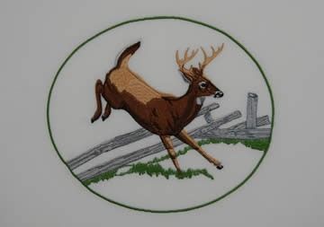 Deer leaping over a wooden fence, embroidered within a green circle.