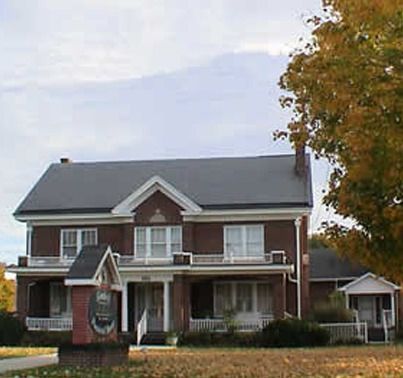 Two-story brick building with white trim, porch, and sign; tree with yellow leaves in the background.
